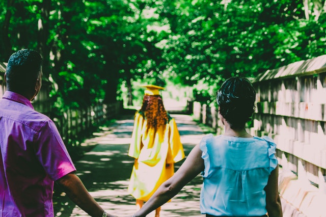 parents walking hand in hand behind their graduating daughter