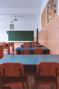 empty classroom with blue tables, brown chairs and blackboard in front