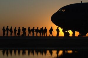 silhouette of a line of soldier loading into an airplane. sun is setting in the background