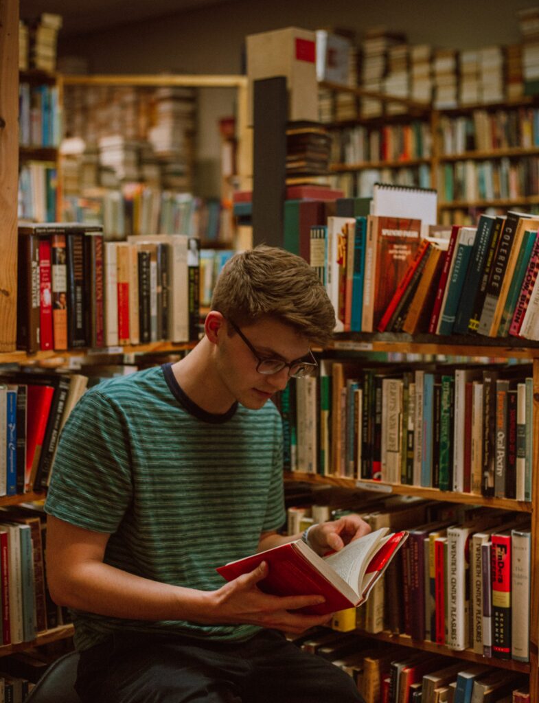 Image of a young man looking at books on a library shelf to show that the reading can click the resources link for Mickie Teaches Students with Disabilities resources